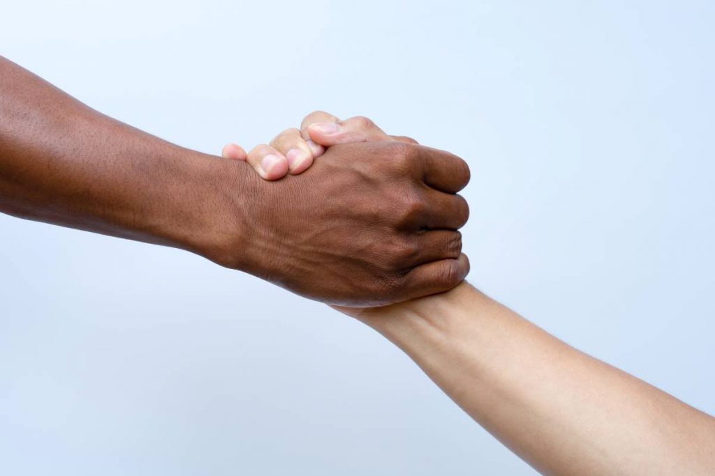 Duas mãos de diferentes em um aperto de mão, representando a solidariedade e o suporte dedicado a pessoas com necessidades específicas em Portugal, como vítimas de violência doméstica, pessoas com deficiência e refugiados.