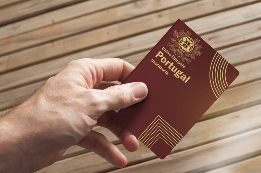Mão segurando um passaporte português, representando as informações sobre emissão e renovação de passaportes em Portugal, inclusive o Passaporte Eletrónico Português e a documentação necessária para viagens internacionais.