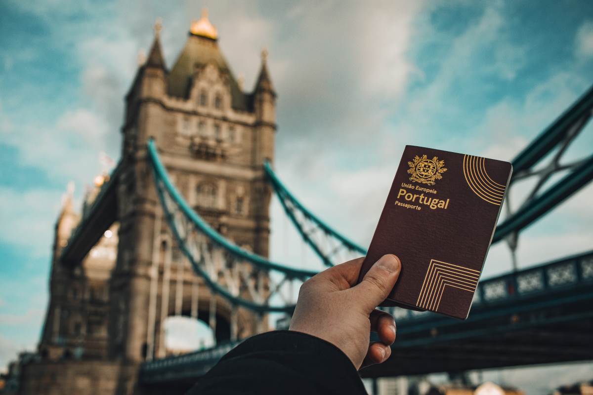 Mão segurando um passaporte português diante da Tower Bridge em Londres, simbolizando cidadãos portugueses pelo mundo