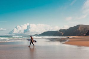 Jovem com prancha de surf na praia em Portugal, representando a possibilidade oferecida pelo visto de trabalho e férias