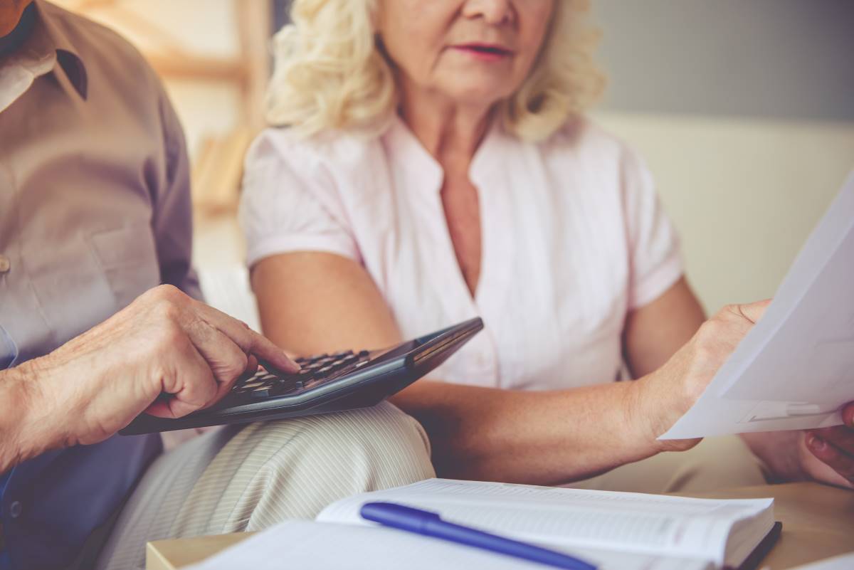 Imagem de um casal de idosos analisando documentos e usando uma calculadora, simbolizando o processo de gestão da pensão de sobrevivência, um apoio financeiro concedido aos familiares após o falecimento de um cônjuge ou familiar.