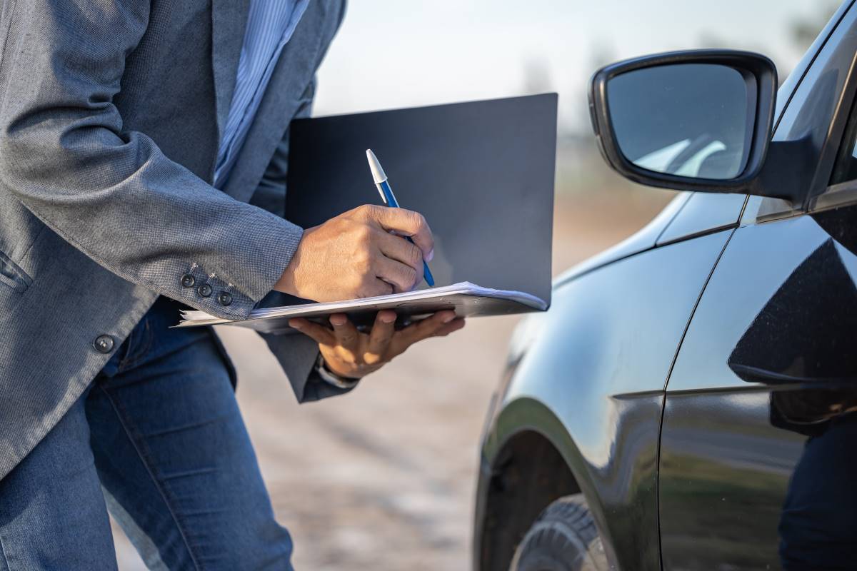 Profissional realizando uma inspeção automóvel, verificando e anotando informações sobre o veículo para garantir conformidade e segurança.