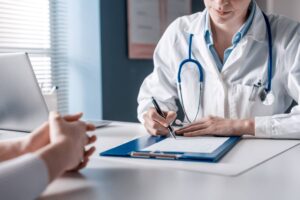 Médico sentado à secretária a preencher um formulário, com um estetoscópio ao redor do pescoço, simbolizando a importância do processo de obtenção do Número de Utente Provisório no sistema de saúde.