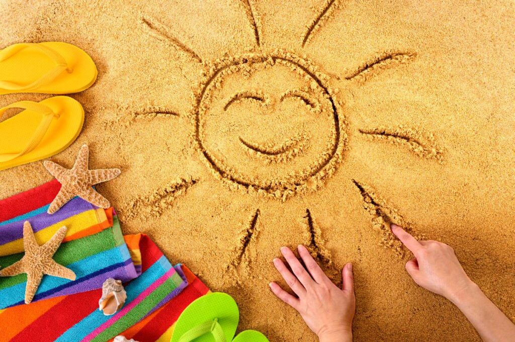 Imagem de um desenho de sol na areia com acessórios de praia, simbolizando a ideia de otimizar as férias em 2025.