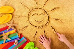 Imagem de um desenho de sol na areia com acessórios de praia, simbolizando a ideia de otimizar as férias em 2025.