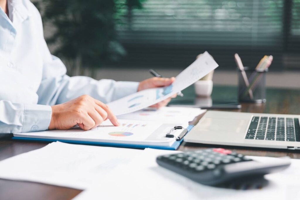 Pessoa a analisar gráficos e relatórios financeiros no escritório, com computador portátil e calculadora sobre a mesa, representando o cálculo e análise do Indexante dos Apoios Sociais (IAS) em Portugal.